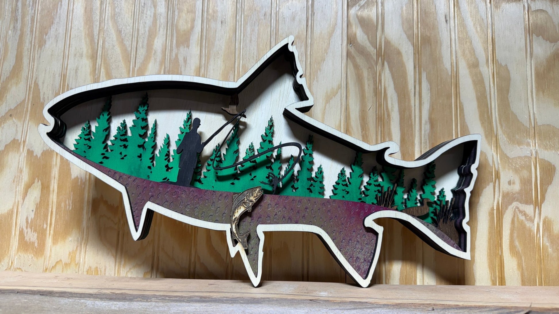 Handcrafted wooden trout wall art by Bunkhouse Studio, featuring a fly fisherman scene, ideal for rustic cabin or lodge décor.