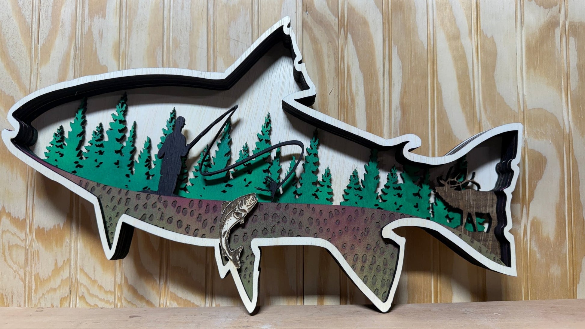 Handcrafted wooden trout wall art featuring a fly fisherman scene, rustic cabin decor, layered animal design by Bunkhouse Studio LLC.